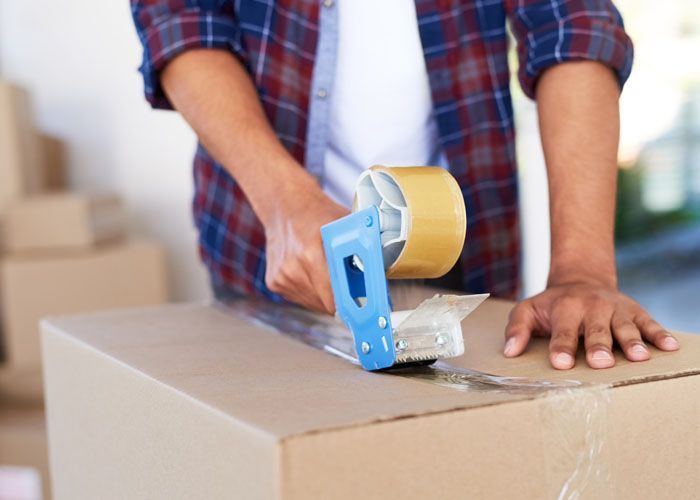 Personne fermant une boîte en carton avec un dérouleur de ruban adhésif.