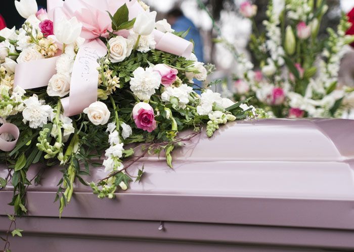 Cercueil rose orné d'une composition florale blanche, rose et verte lors de funérailles.