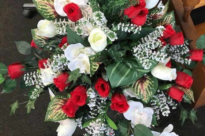 Composition florale rouge et blanche, avec des feuilles vertes, sur un fond sombre.