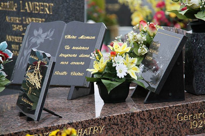 Pierres tombales fleuries. Monument commémoratif en granit noir avec inscriptions dorées. Compositions florales colorées. 