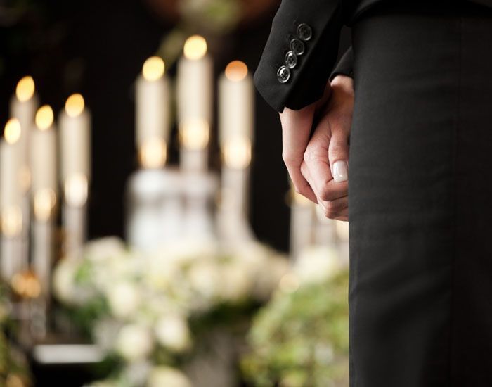 Une personne en costume noir tient les mains près des bougies au mémorial.