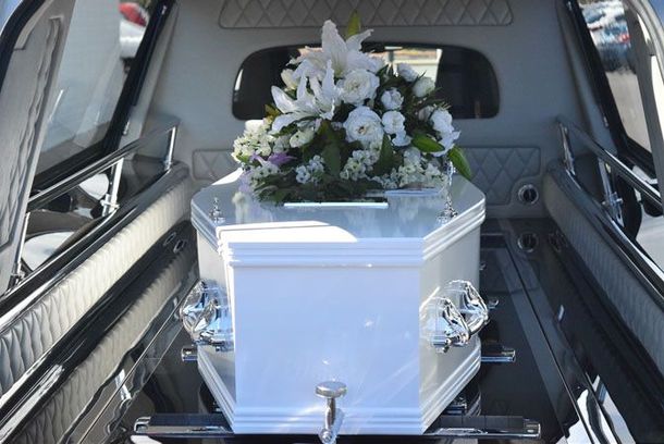 Cercueil blanc avec composition florale à l'intérieur d'un corbillard.