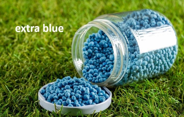 Un frasco de fertilizante azul se encuentra encima de un exuberante campo verde.