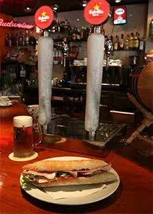 Un sándwich y un vaso de cerveza están sobre una mesa en un bar.