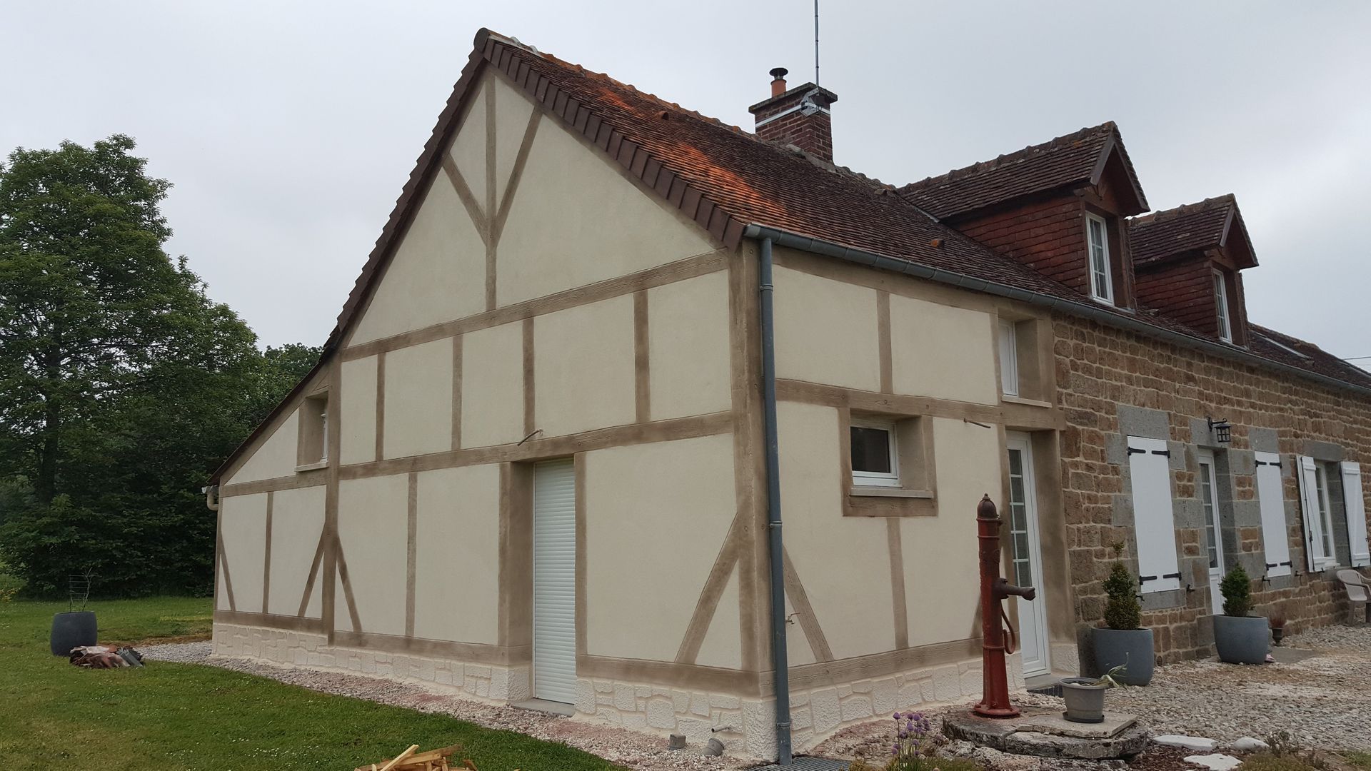 Maison à colombages rénovée, aux murs crème et au toit rouge, sur un terrain verdoyant