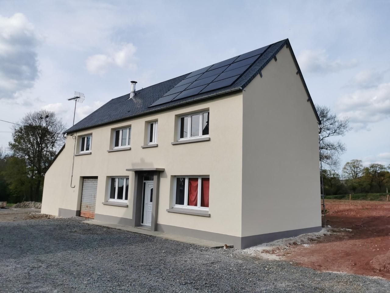 Maison à deux étages avec panneaux solaires sur le toit, extérieur beige clair, finitions grises, allée en gravier et ciel nuageux.