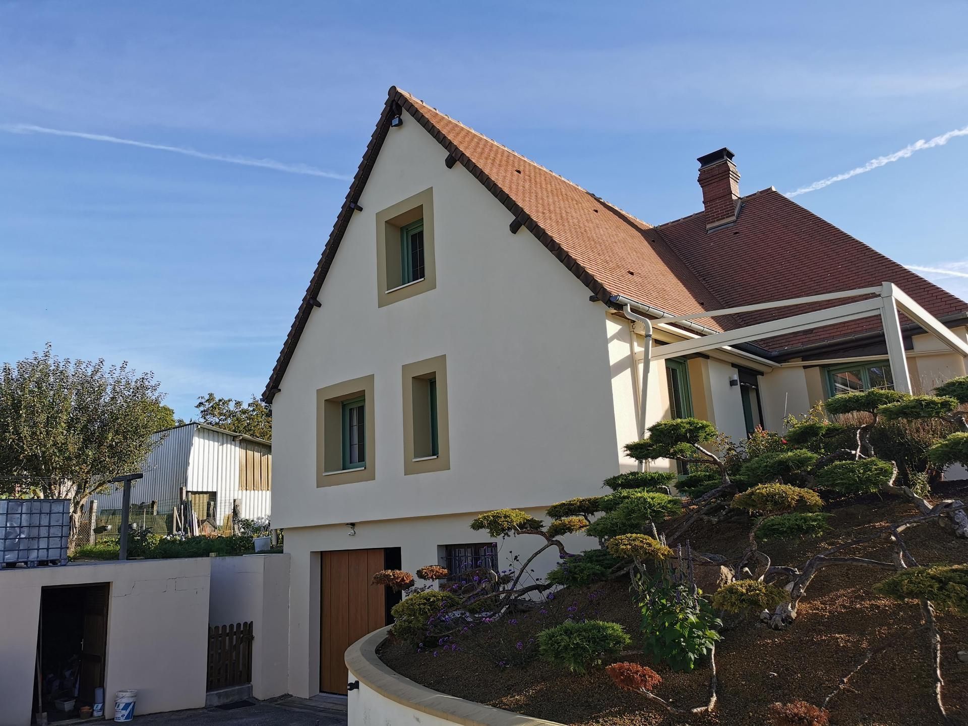 Maison blanche au toit de tuiles rouges et au jardin bien entretenu, sous un ciel bleu dégagé