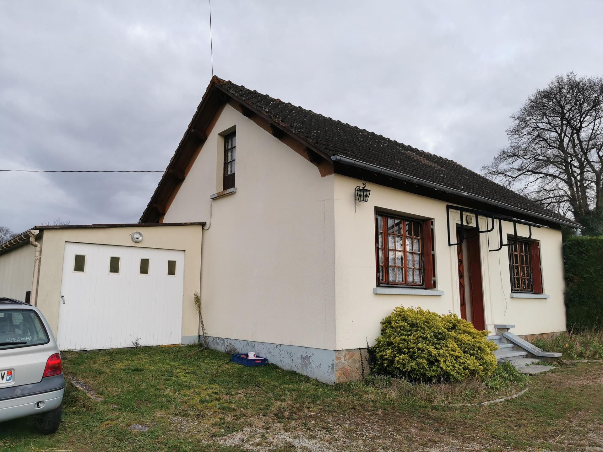 Maison beige avec garage, toit marron et encadrements de fenêtres sombres sous un ciel nuageux.