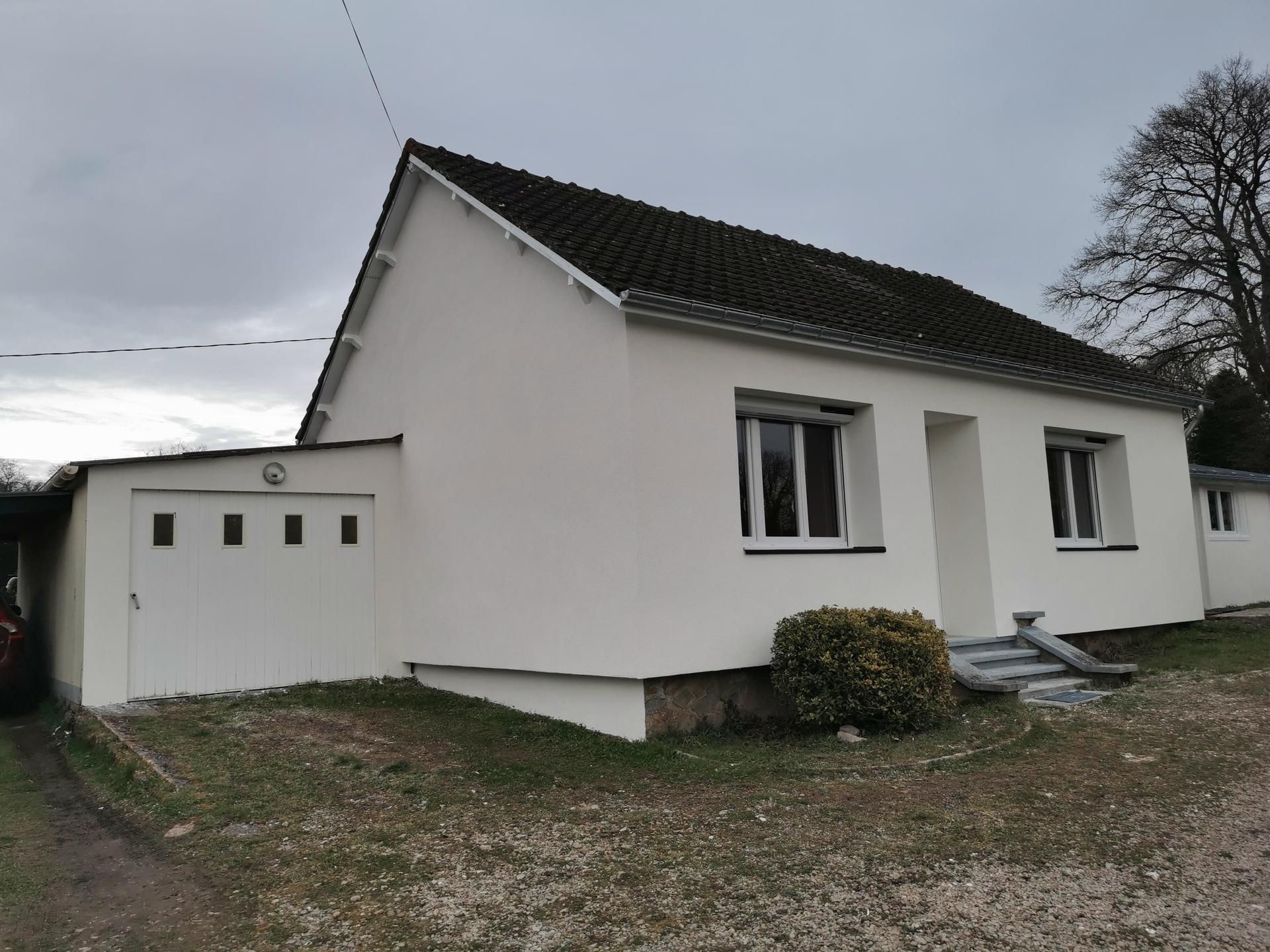Maison blanche de plain-pied avec garage, sous un ciel nuageux.