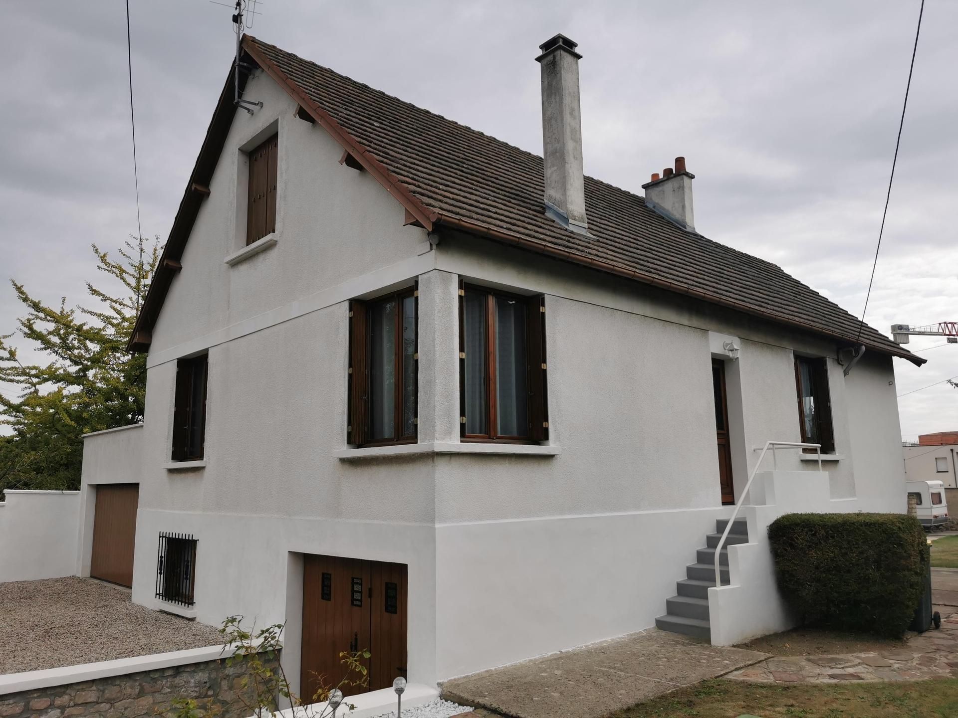 Maison blanche à deux étages avec un toit gris, des portes marron et un escalier extérieur par temps nuageux