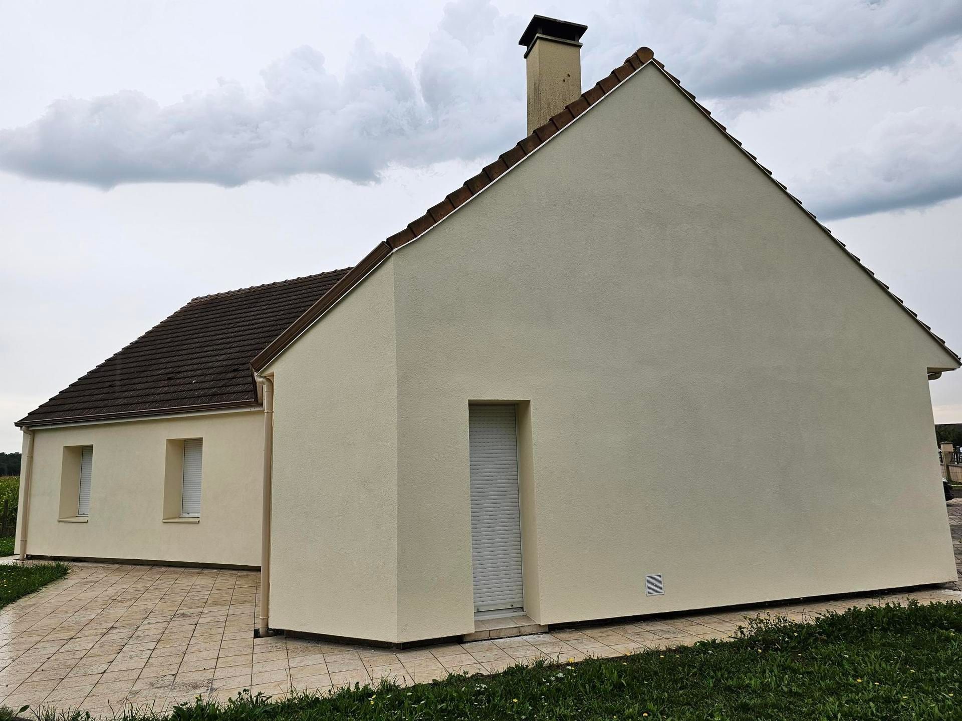 Petite maison blanche au toit sombre et à la cheminée, vue de côté sous un ciel nuageux