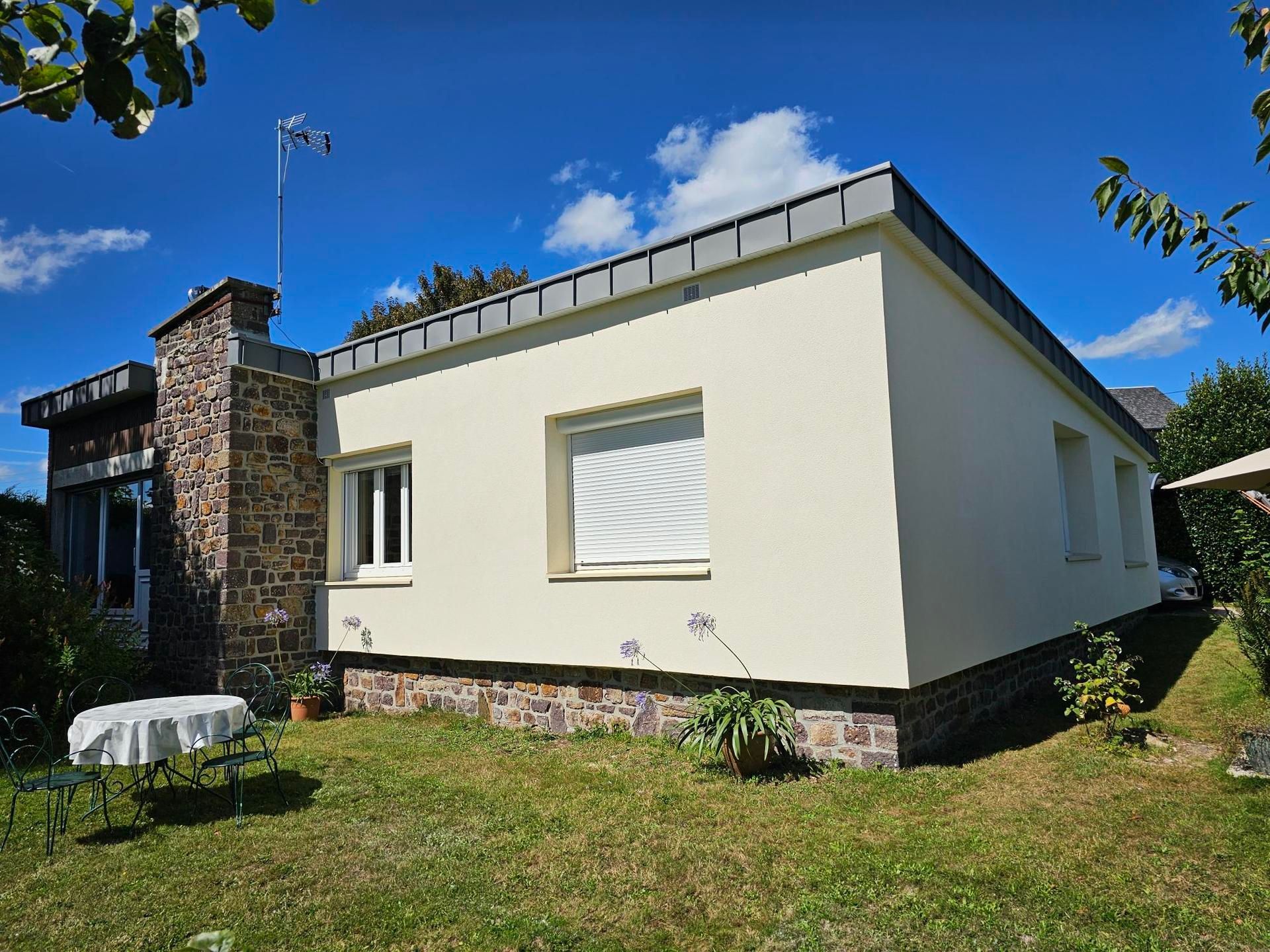 Une maison couleur crème avec des touches de pierre sur une pelouse verdoyante sous un ciel bleu.