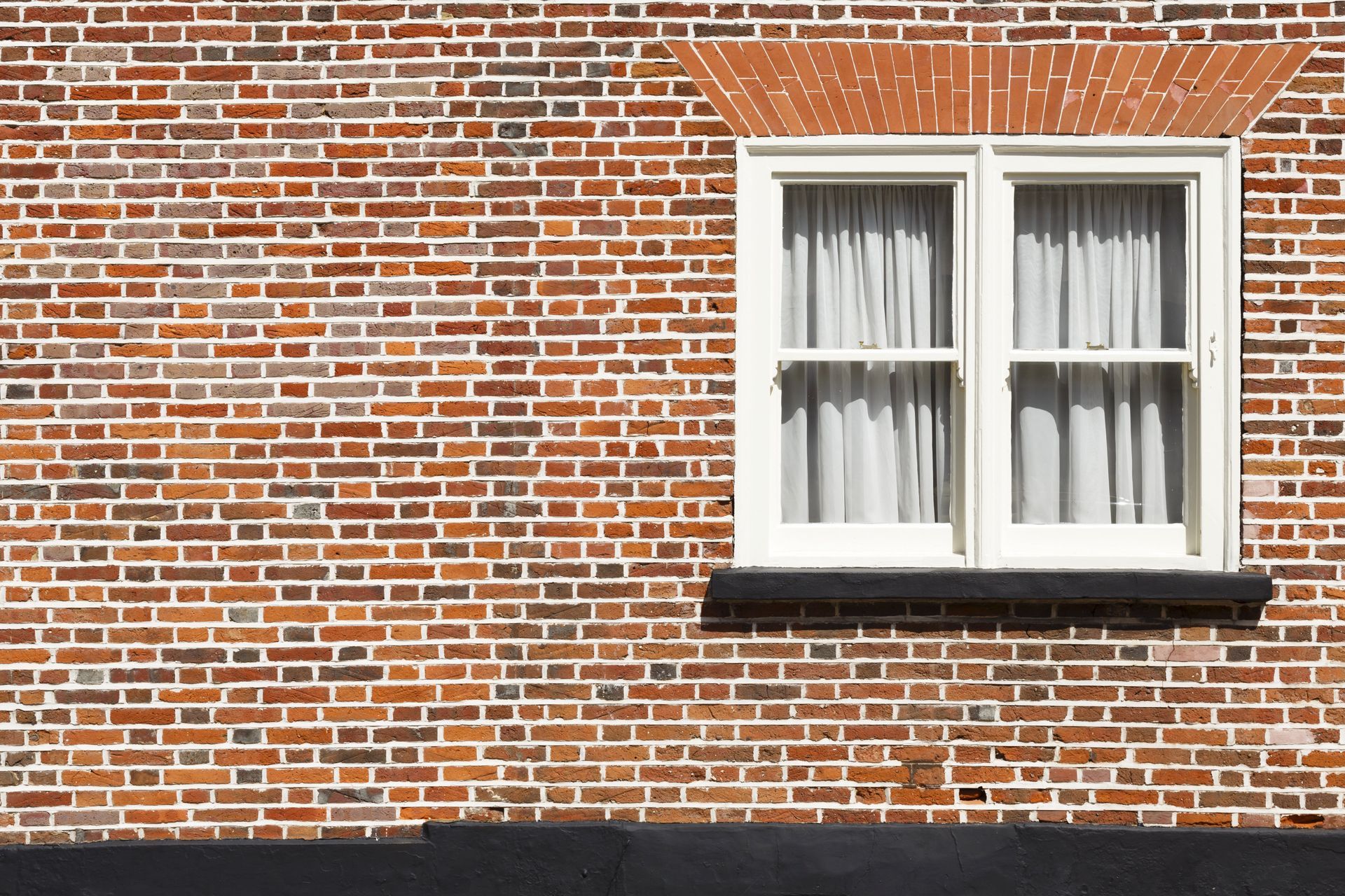 Mur en briques avec une fenêtre encadrée de blanc et des rideaux au-dessus d’un rebord sombre.