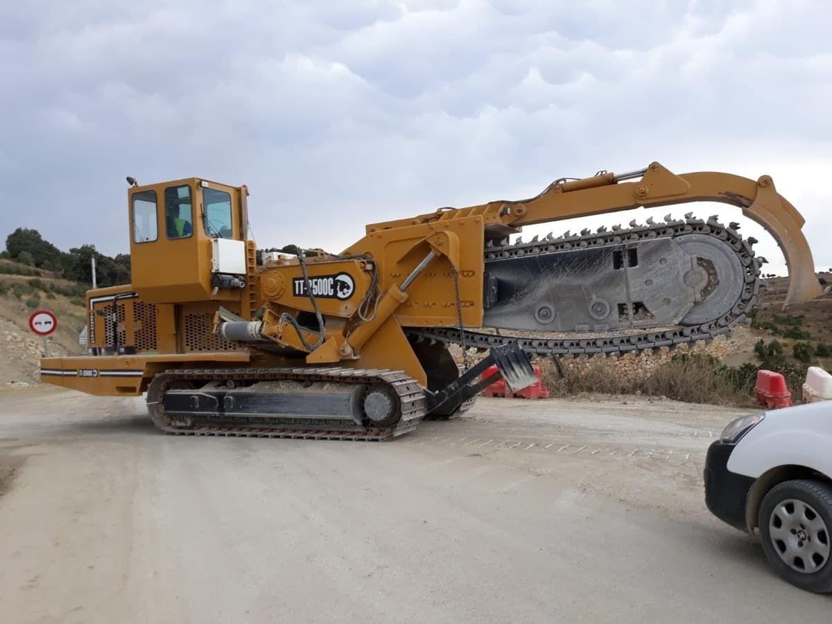 Un gran tractor amarillo está estacionado junto a una camioneta blanca en un camino de tierra.