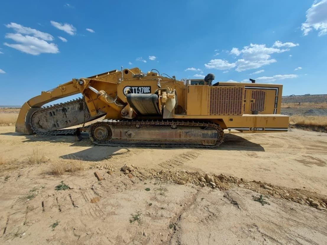 Una gran excavadora amarilla está sentada en el medio de un campo de tierra.