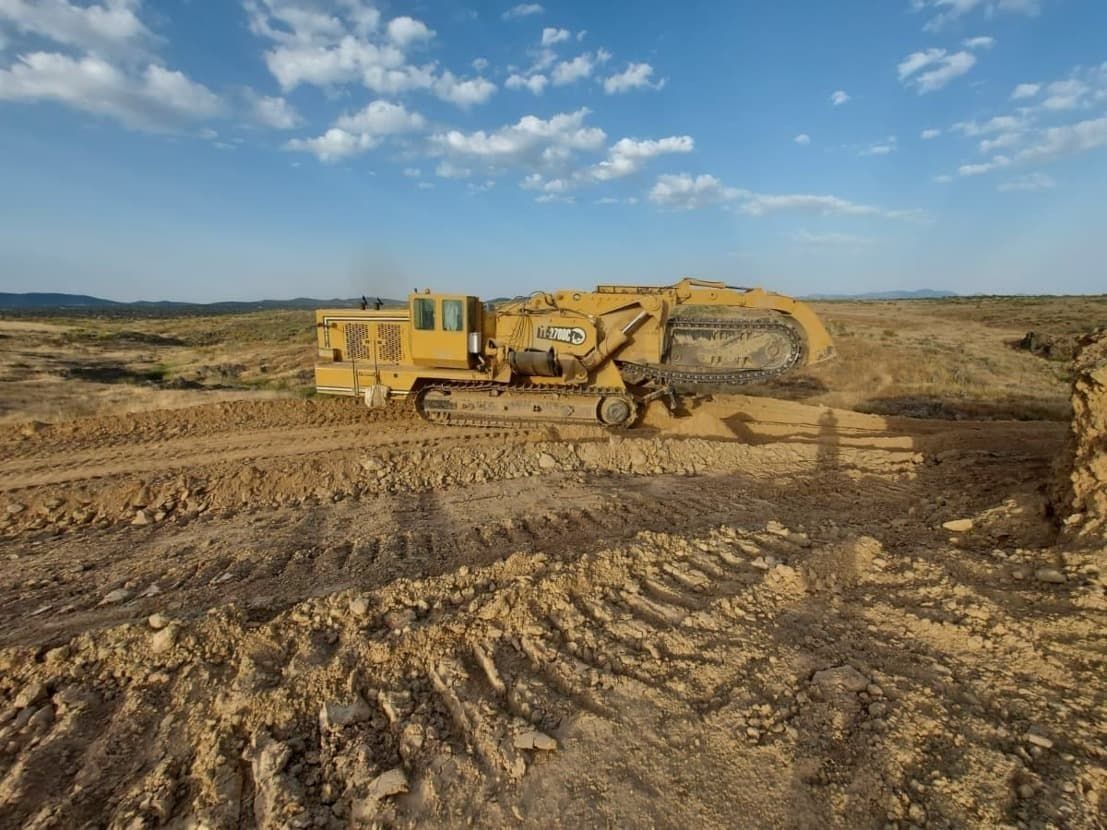 Una excavadora amarilla avanza por un campo de tierra.
