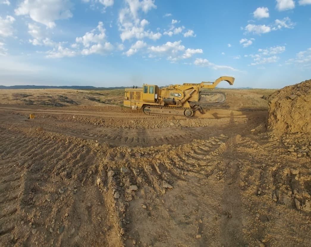 Una excavadora amarilla avanza por un campo de tierra.