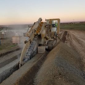Una excavadora está cavando una zanja al costado de un camino de tierra.
