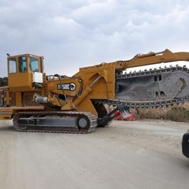 Una excavadora amarilla con una motosierra acoplada está estacionada al costado de un camino de tierra.