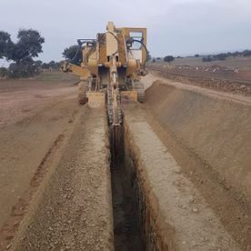 Un tractor amarillo está cavando una zanja al costado de un camino de tierra.