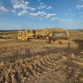 Una excavadora amarilla avanza por un campo de tierra.