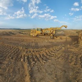 Una excavadora amarilla avanza por un campo de tierra.