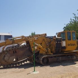 Una excavadora amarilla está estacionada en un terreno de tierra al lado de un poste verde.
