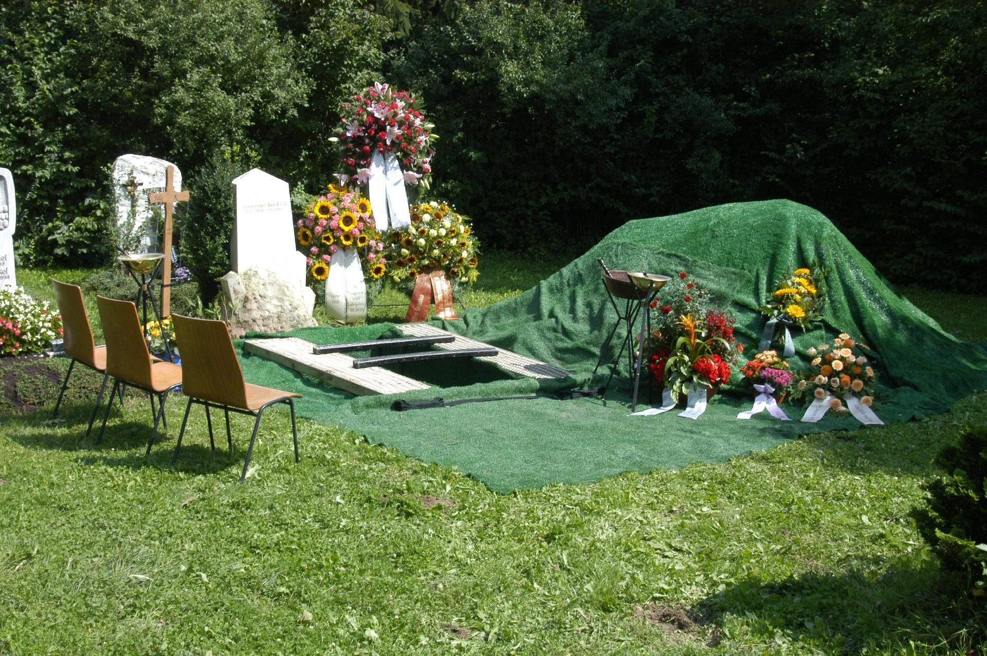 Ein Grab ist mit einer grünen Plane und Blumen bedeckt