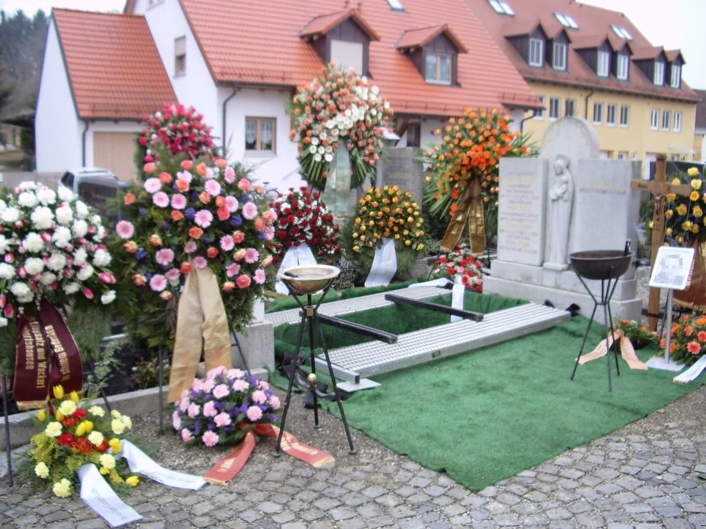 Ein von Blumen und Bändern umgebenes Grab vor einem Haus