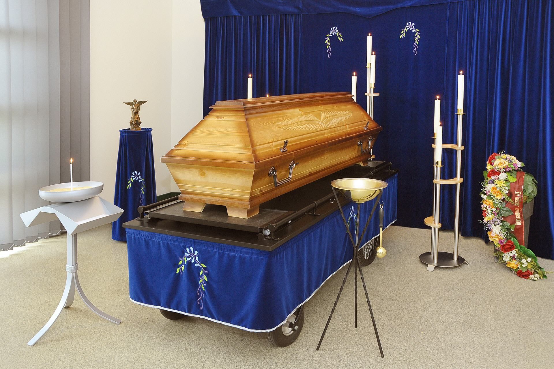 Ein Sarg steht auf einem Wagen in einem Raum mit blauen Vorhängen