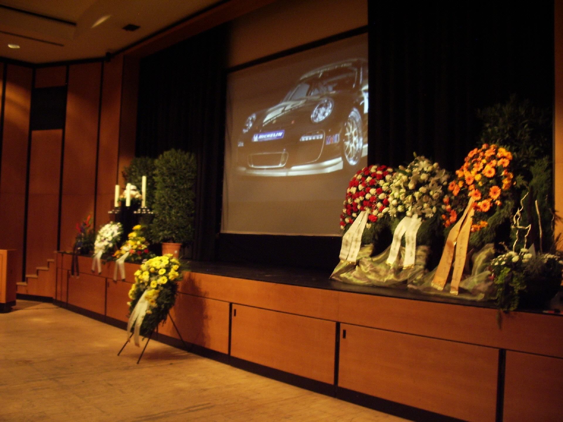 Eine Bühne mit Blumen und einer Projektionsleinwand, auf der ein Auto zu sehen ist