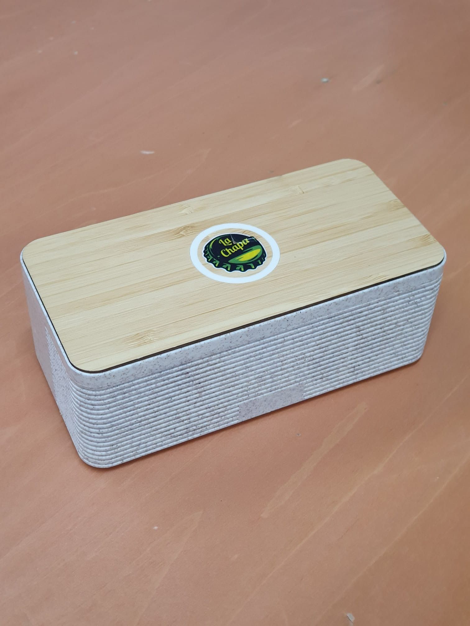 Un altavoz blanco con tapa de madera está sobre una mesa de madera.