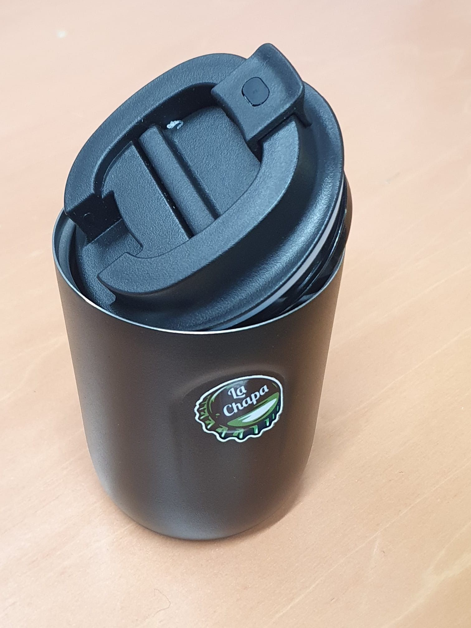 Una taza de café negro con tapa está sobre una mesa de madera.