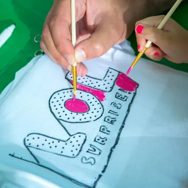 Una persona está pintando Lol Surprise en una camisa blanca.