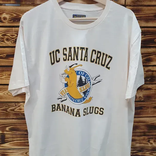 Una camiseta blanca de los Banana Slugs de la Universidad de California en Santa Cruz está colgada en una percha.