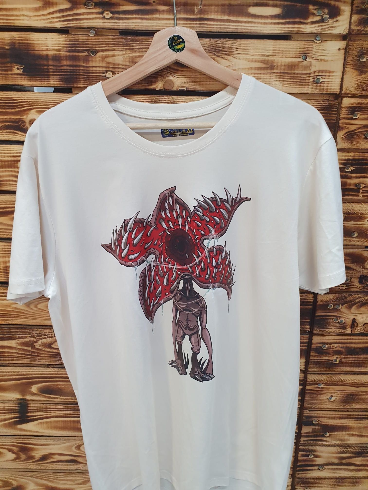 Una camiseta blanca con una flor roja cuelga de una percha de madera.