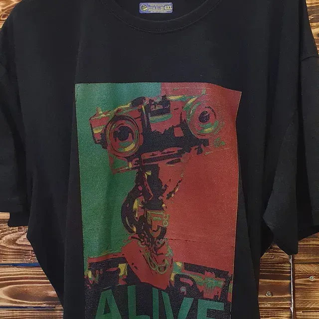 Una camiseta negra con la imagen de un robot está colgada en una pared de madera.