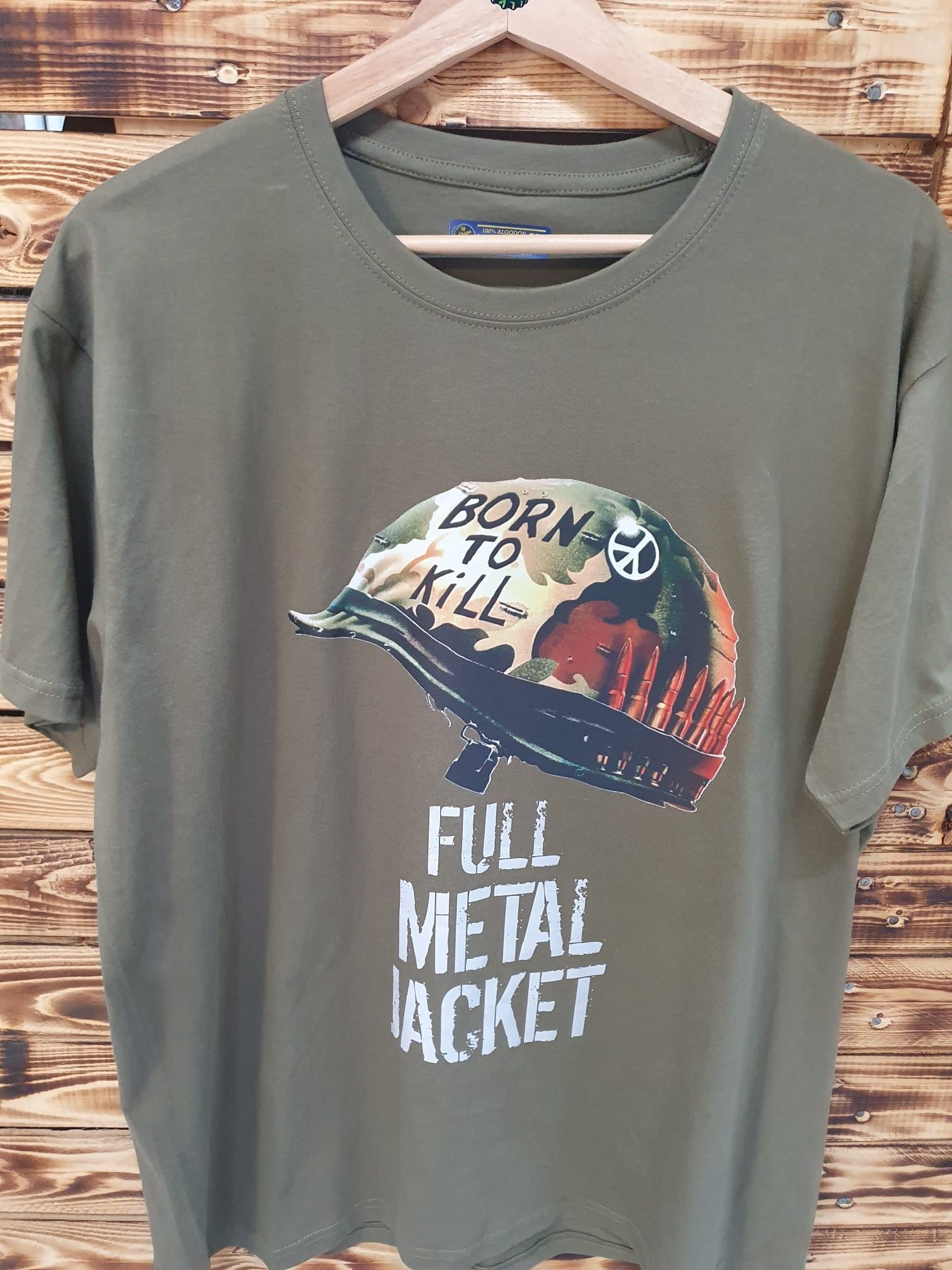 Una camiseta verde con un casco está colgada en una percha de madera.