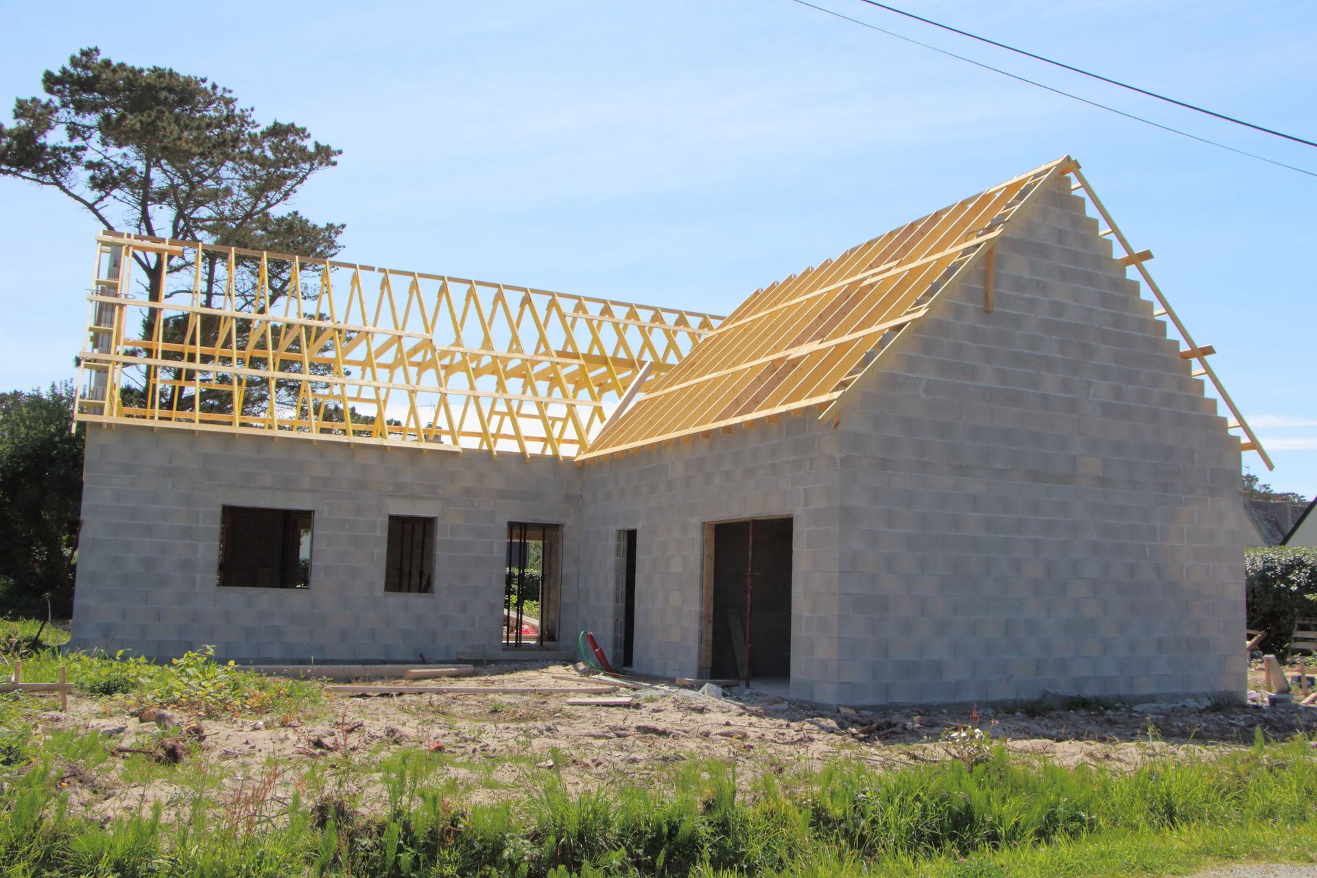 Maison en construction avec murs en parpaings et charpente industrielle en bois.