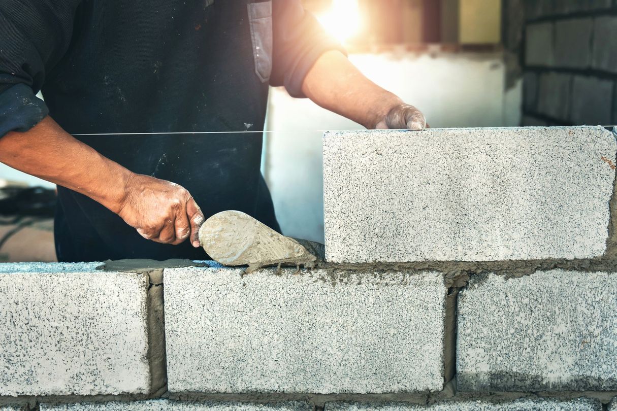 Des mains étalent du mortier tout en empilant des parpaings sur un chantier de construction.