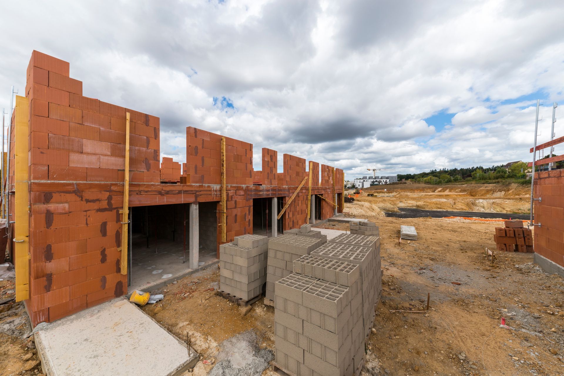 Maison en briques partiellement construite, avec des blocs de béton empilés au premier plan.