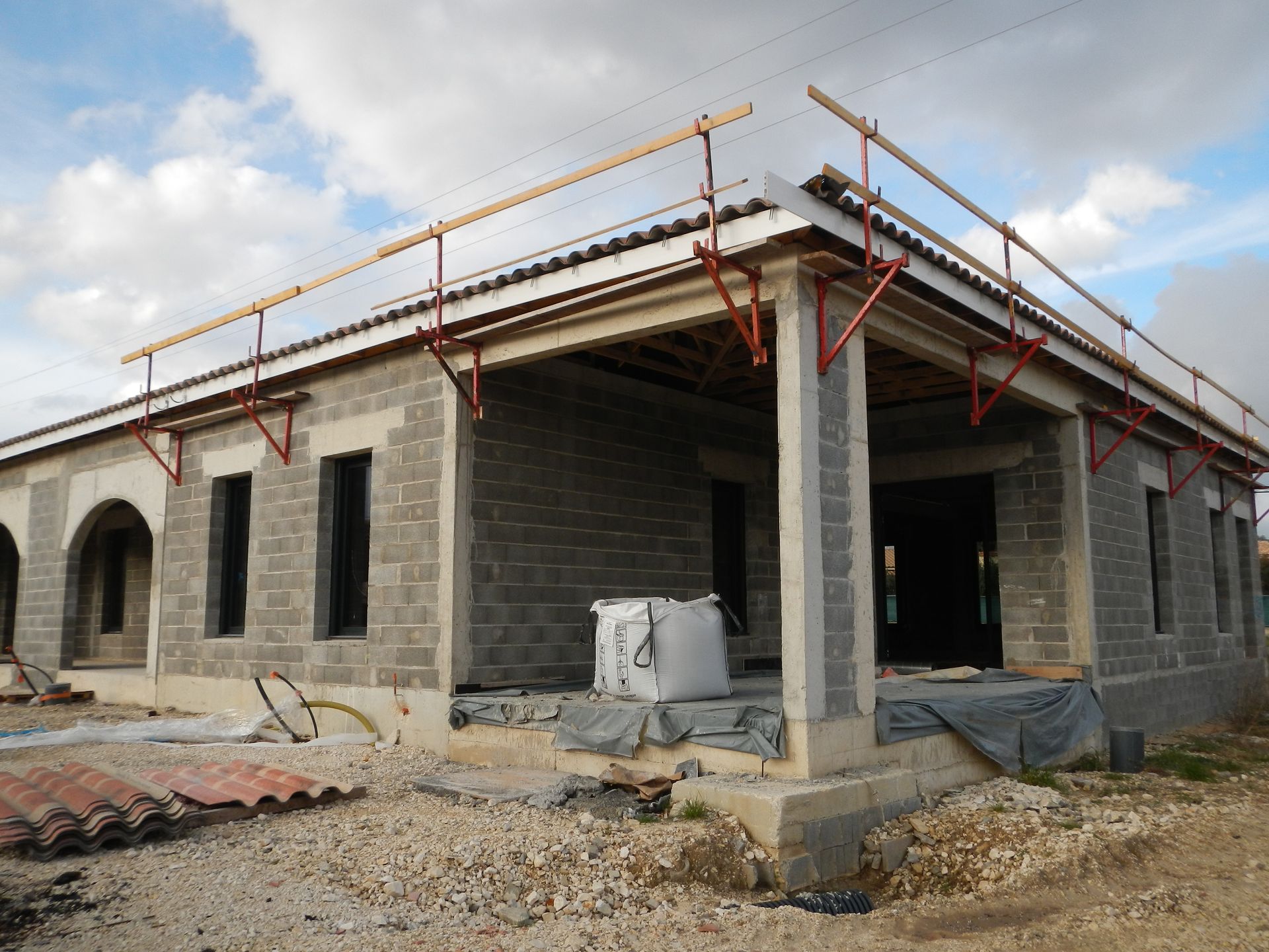Chantier de construction d’une maison en parpaings avec toiture en cours, échafaudage en place et matériaux au sol.