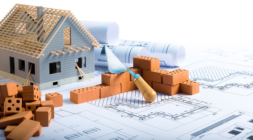 Maison partiellement construite avec ossature en bois, briques et plans architecturaux enroulés.