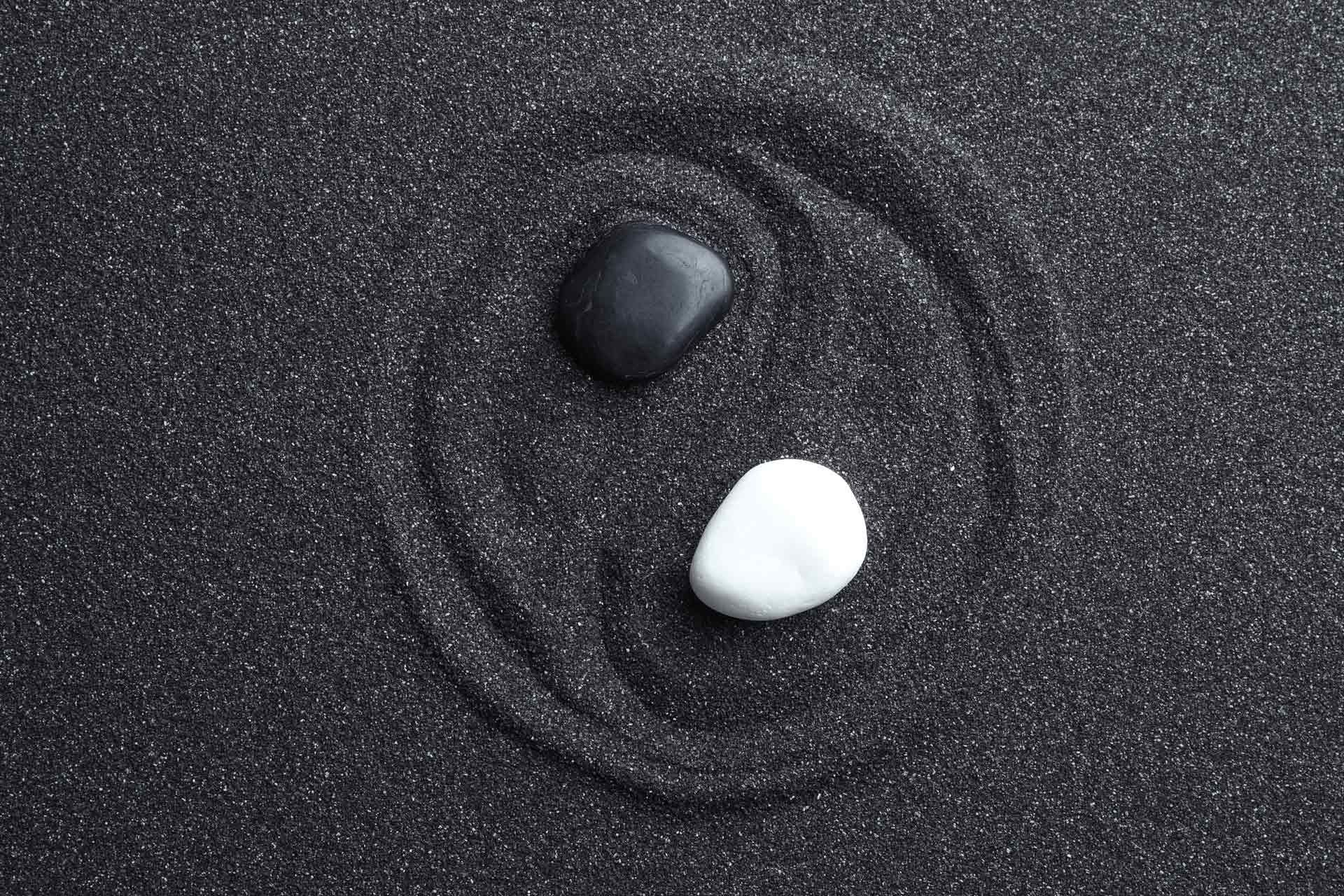 Galets noir et blanc sur sable noir représentant le Yin Yang