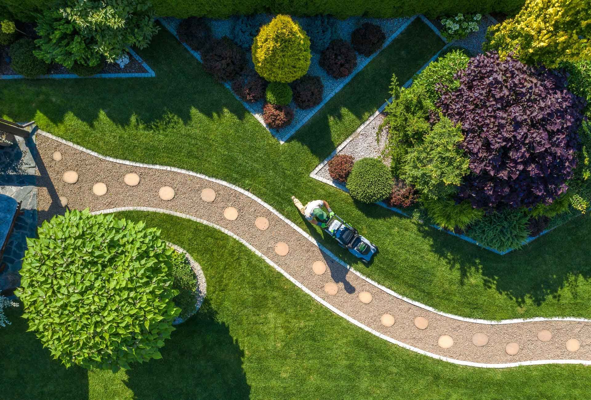 Vue aérienne d'un jardinier tondant une pelouse autour de massifs entretenus