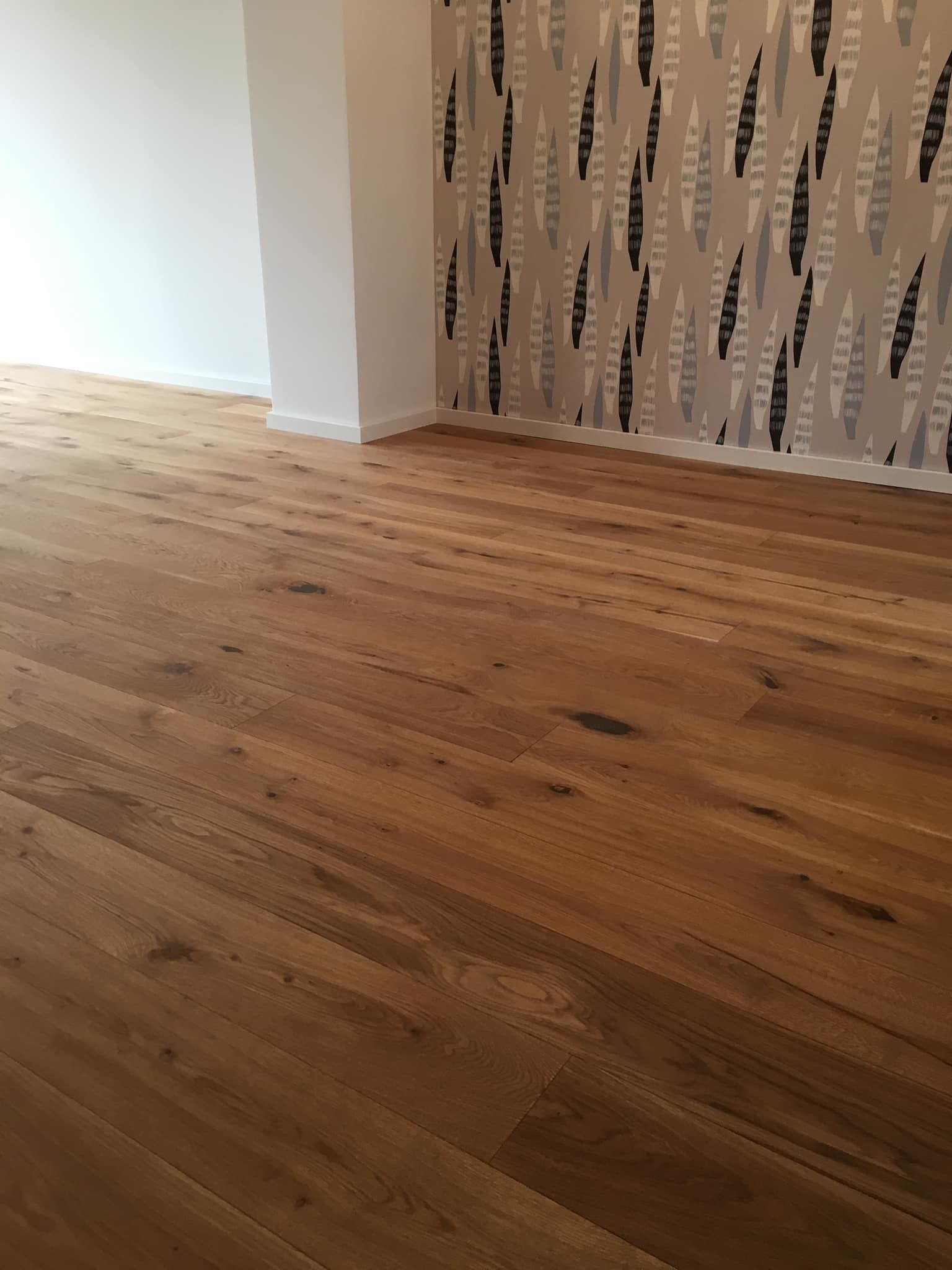 Ein leerer Raum mit einem Holzboden und einer Tapete mit Blättern darauf