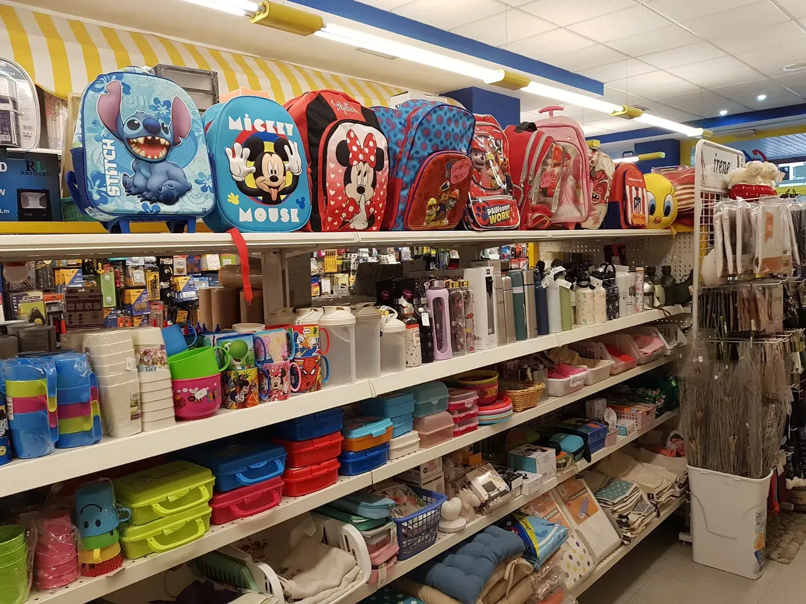 Estantes de una tienda llenos de útiles escolares: mochilas, botellas de agua y loncheras en varios colores y diseños de personajes.
