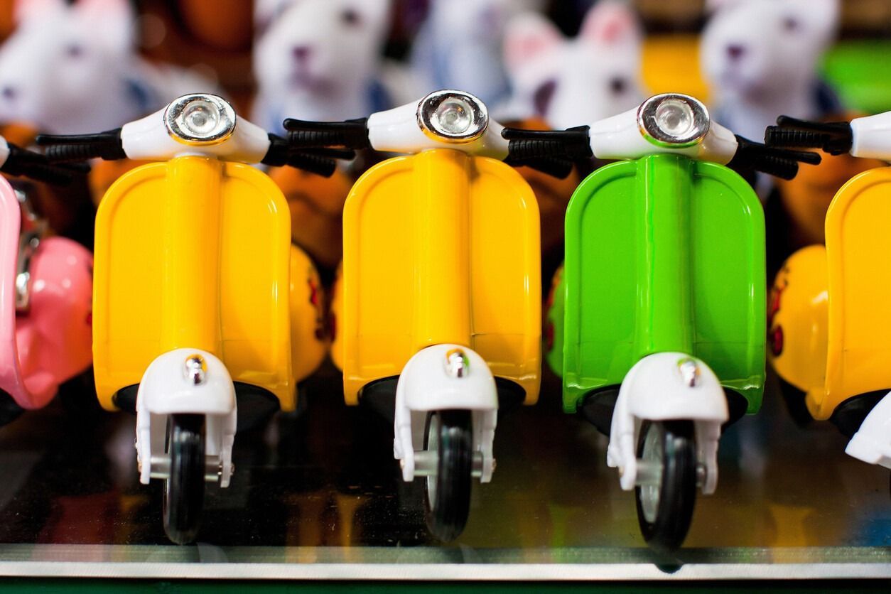 Patinetes de juguete de colores en fila; destacan los colores rosa, amarillo y verde. Faros blancos y manillar negro.