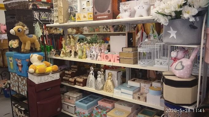 Estantes llenos de diversos artículos decorativos, como cajas, figuras, peluches y arreglos florales en un entorno de tienda.
