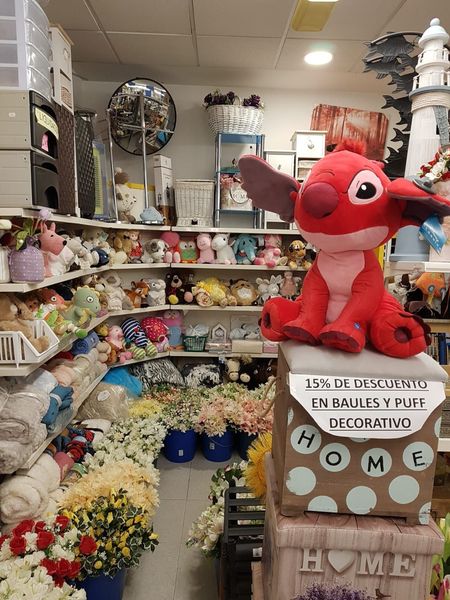Una tienda minorista llena de decoraciones y juguetes de peluche, incluido un gran animal de peluche rojo de Stitch en una caja decorativa.